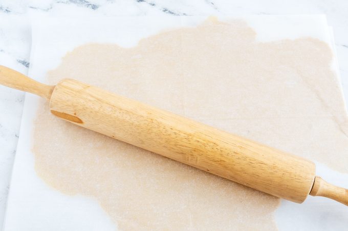Tagalongs dough rolled out between sheets of parchment paper; a rolling pin sits on top