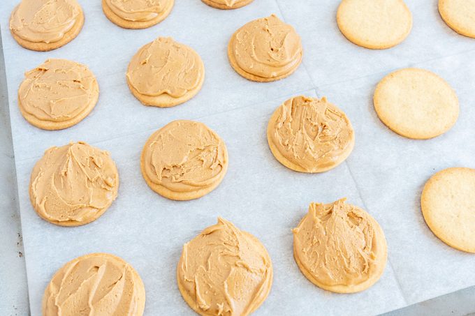 Tagalongs on a baking sheet; some have peanut butter topping, some do not yet have peanut butter topping