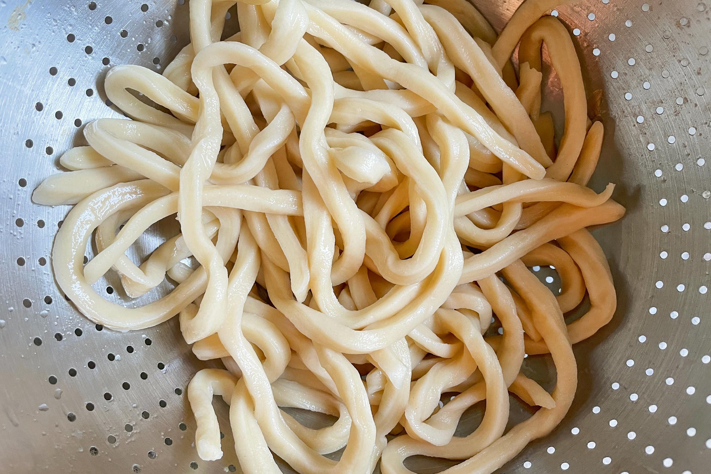 cooked udon noodles in a metal collander