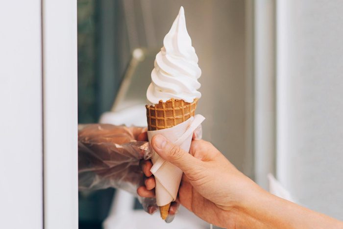 annonymous hand receiving a vanilla ice cream cone from a window