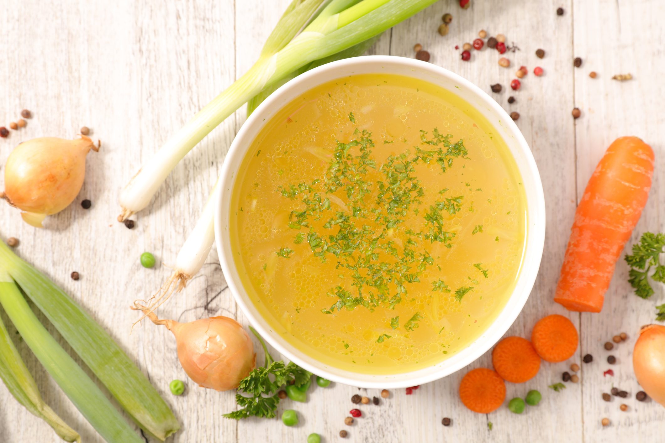 vegetable broth in bowl surrounded by fresh vegetables