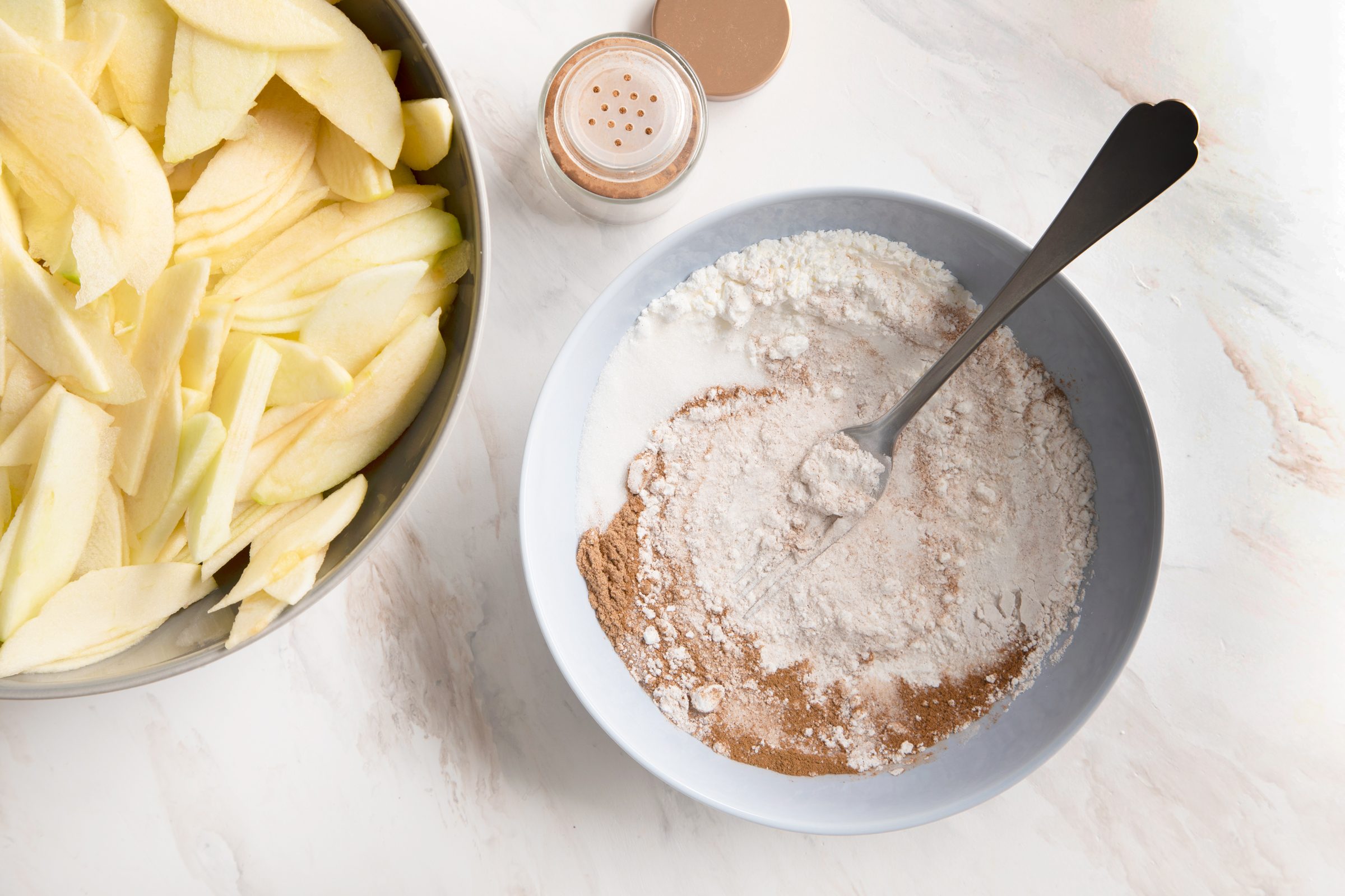 a apple pie cinnamon sugar mix in a small bowl with a fork and the bowl with sliced apples off to the side