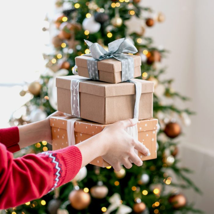 Young woman's hand holding Christmas presents indoors.