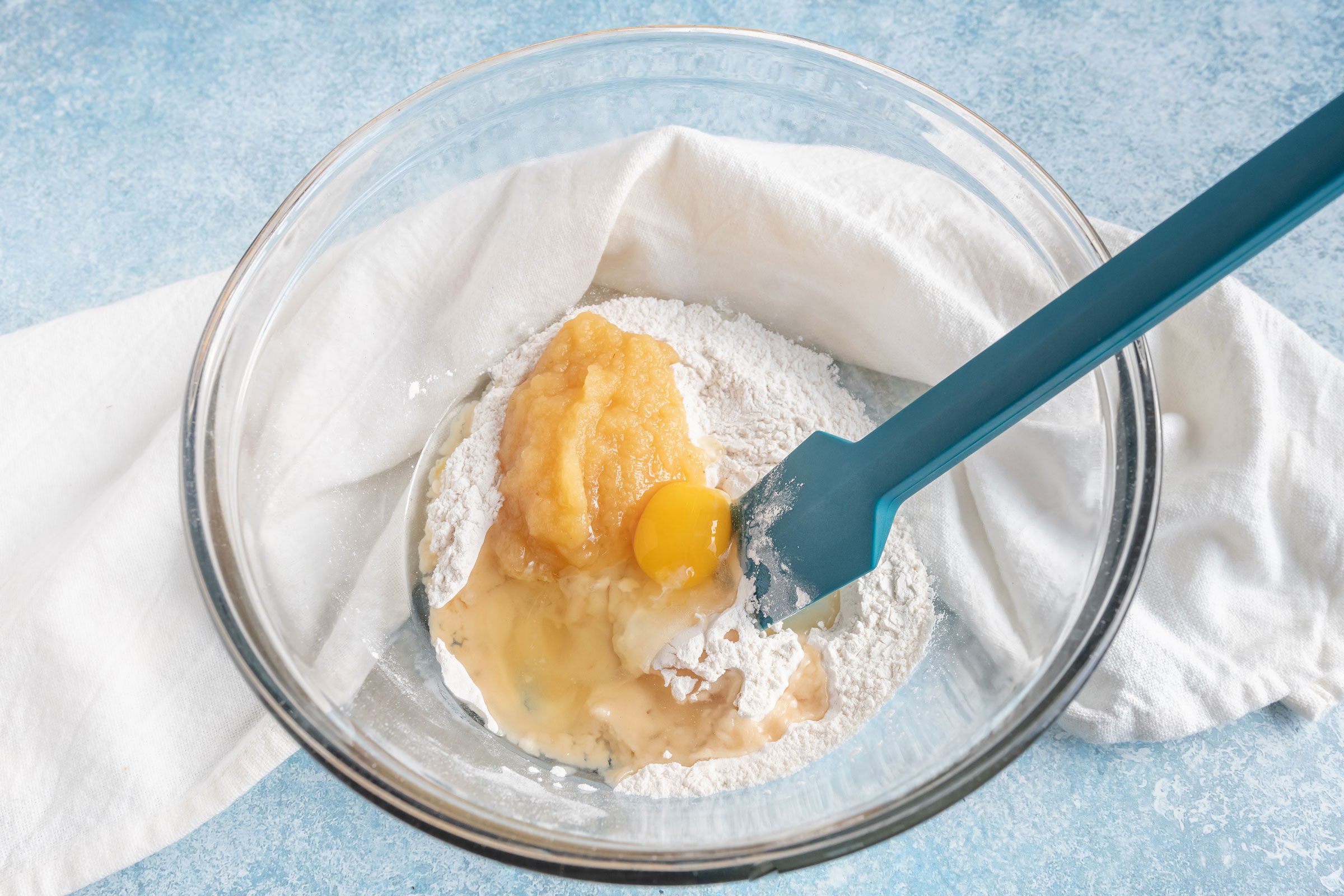 mixing batter for dog cupcakes a glass bowl with a rubber spatula on a blue countertop