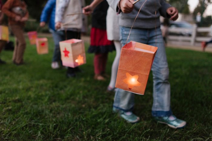 Low section of children carrying illuminated paper lanterns while walking on field