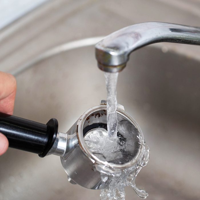 Cleaning the coffee maker's horn under the water of the water tap, close-up. Caring for the coffee machine parts