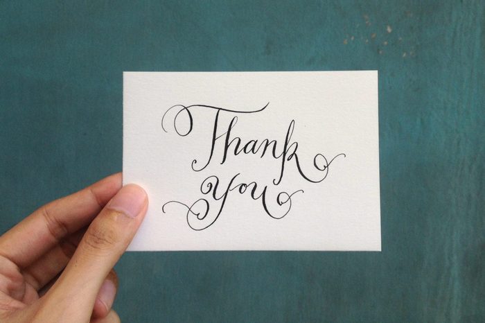 Close-Up Of Hand Holding Paper With Thank You Text Against Wall