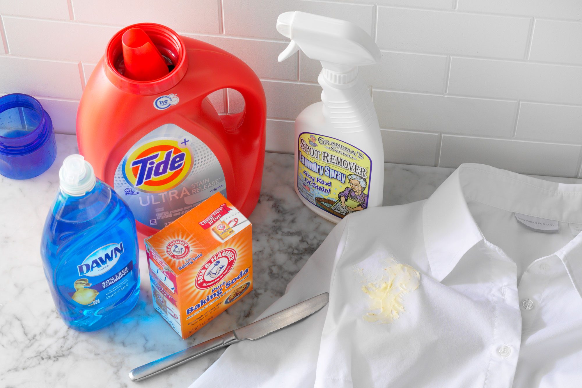 White Shirt with butter stain next to stain removal supplies on white marble kitchen counter top