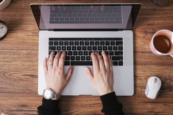 Woman's hands working on laptop at home office, top view