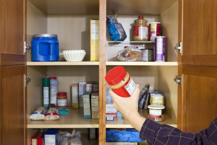 Close up of a woman's hand taking a jar of peanut butter out of an open pantry.