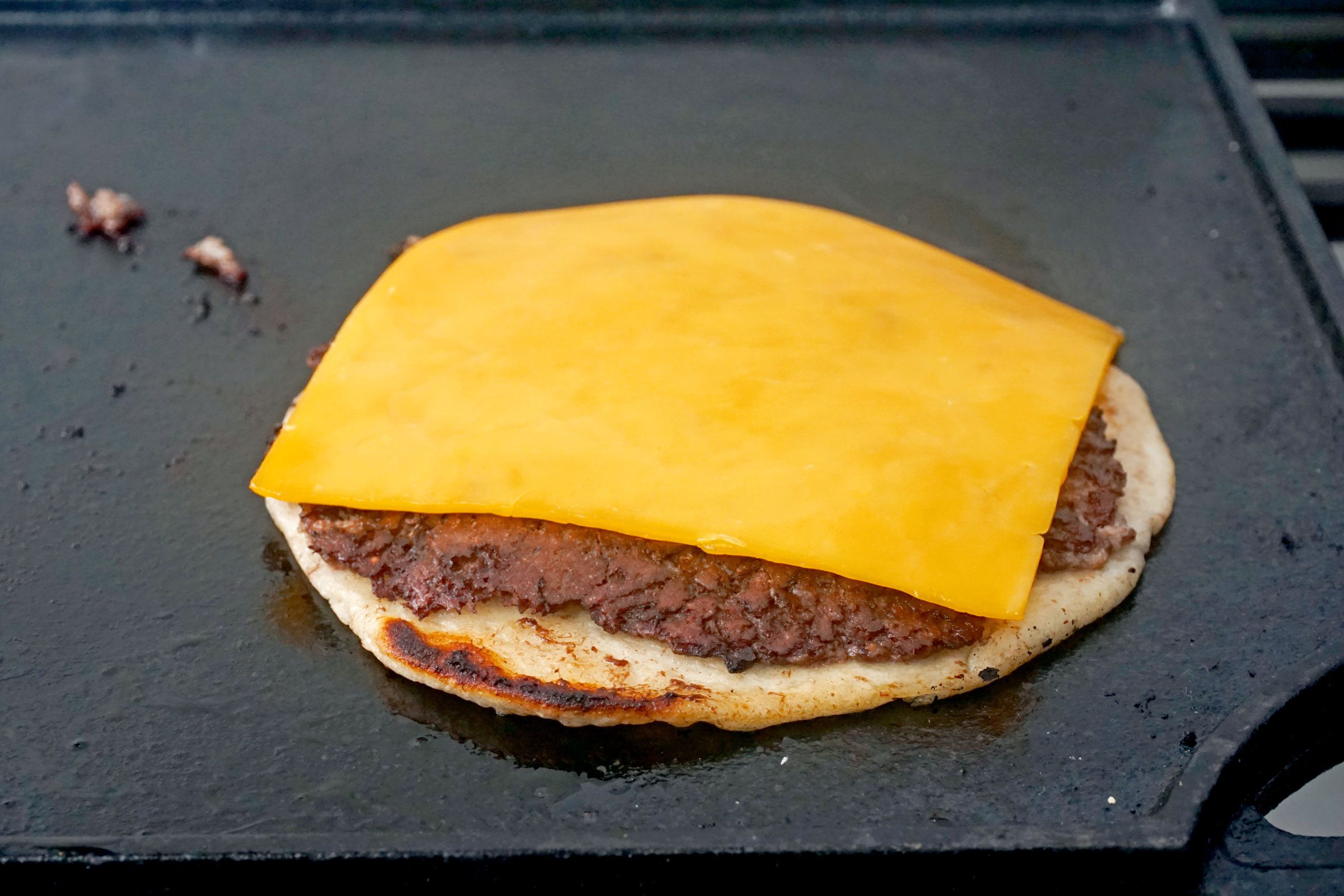 Smash Burger on tortilla with cheese on the griddle