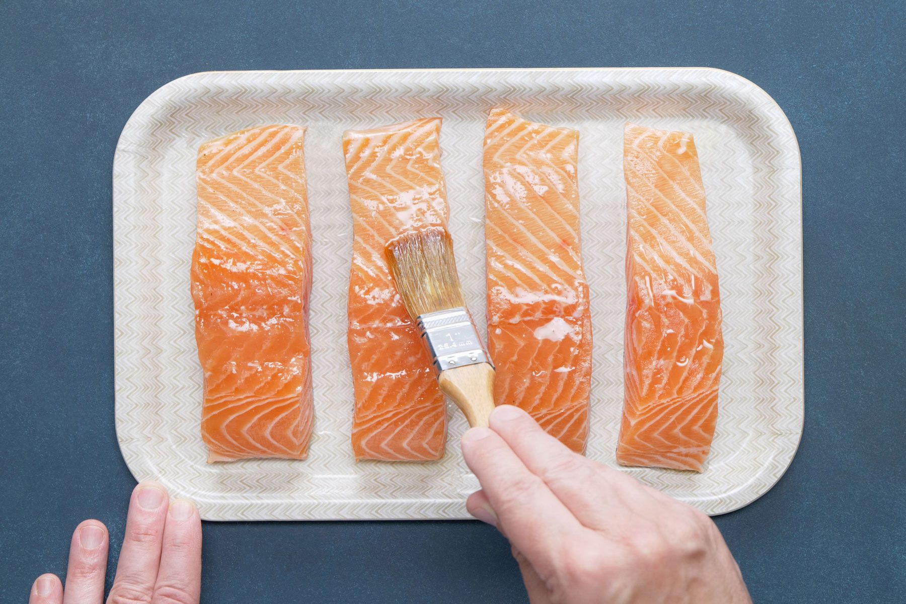A person brushing olive oil over the salmon fillets