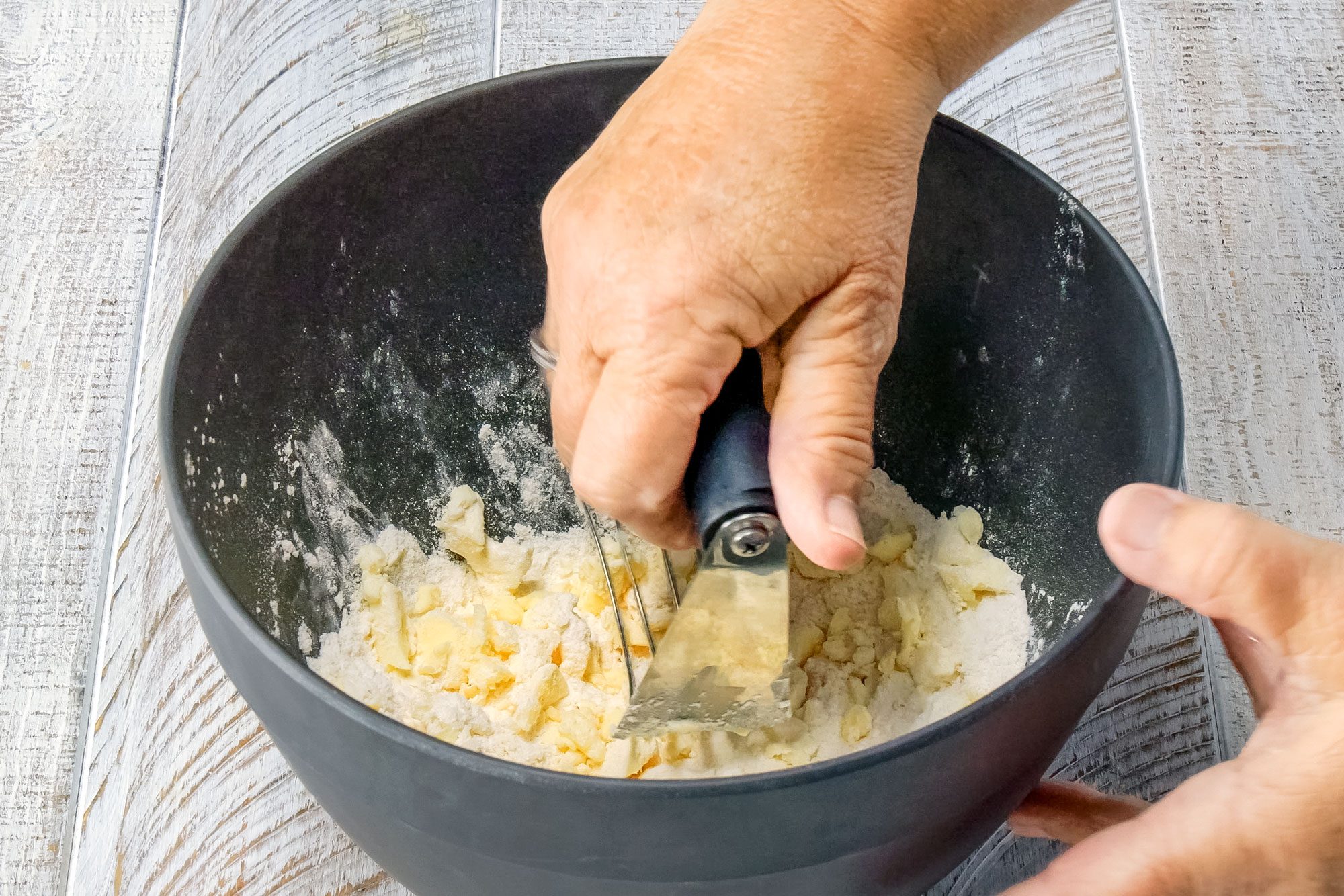 Mixing flour, sugar, salt and cold butter in a black bowl to make dough for Blueberry Tart on Wooden Surface