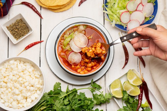 Red pozole with chicken and hominy on white background