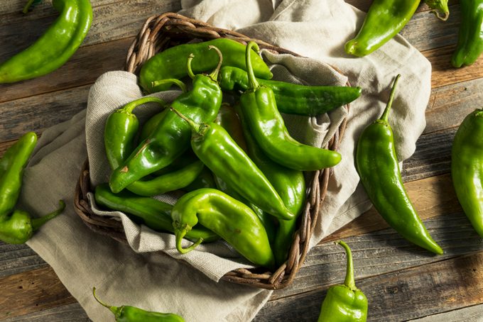 Raw Green Spicy Hatch Peppers in a wooden basket on a towel on the countertop