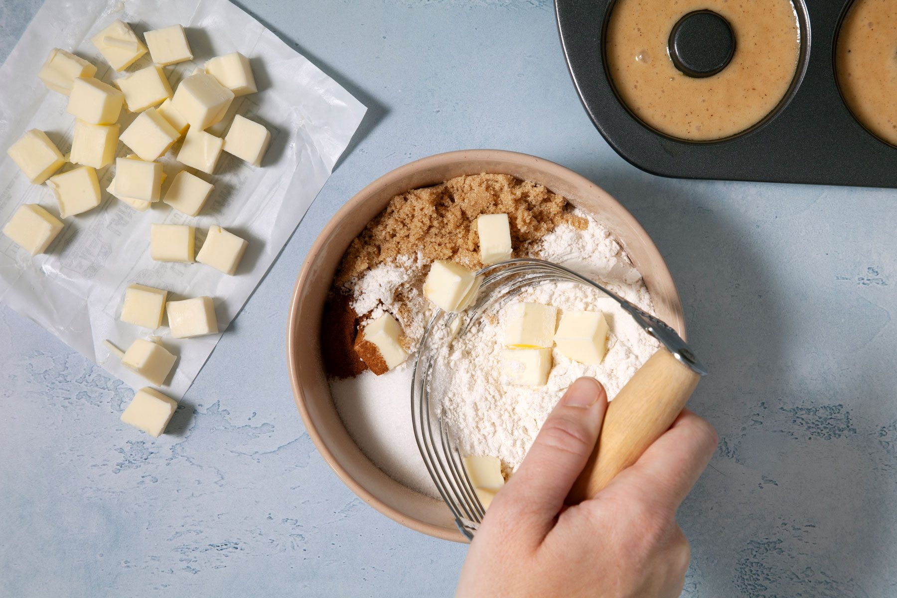 A Person Holding a Whisk to a Bowl of Flour and Butter