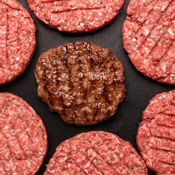 Raw and Grilled Hamburger patties top view on black table