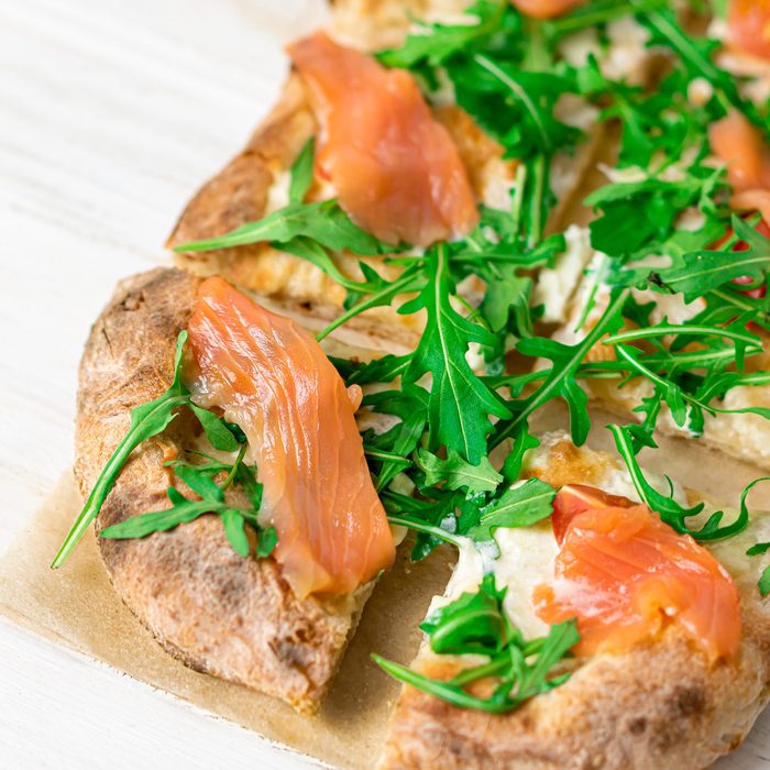 Roman pizza with salmon cut in pieces and served on a white wooden board. Traditional roman pizza with fish.