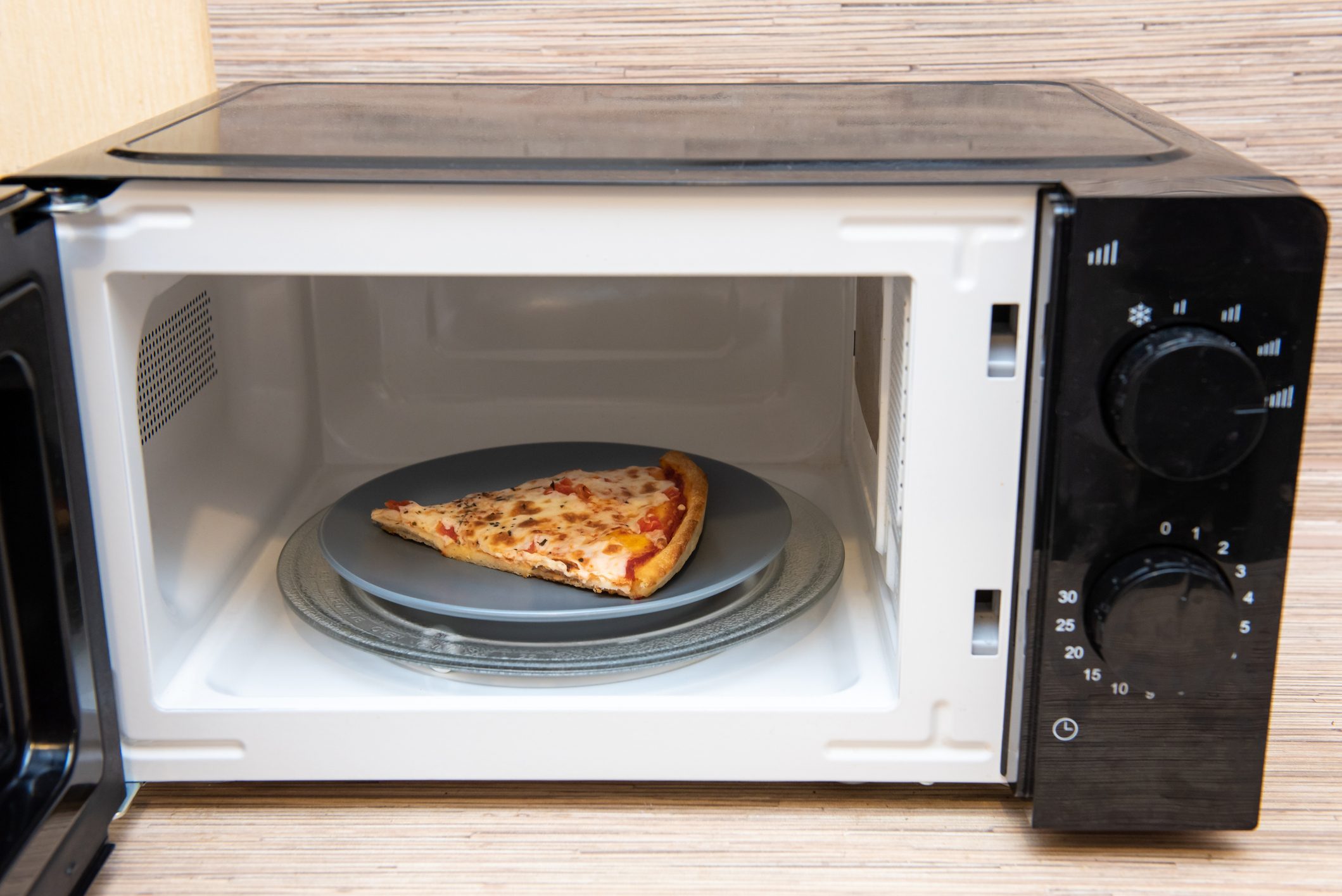 Plate with slice of pizza in microwave oven