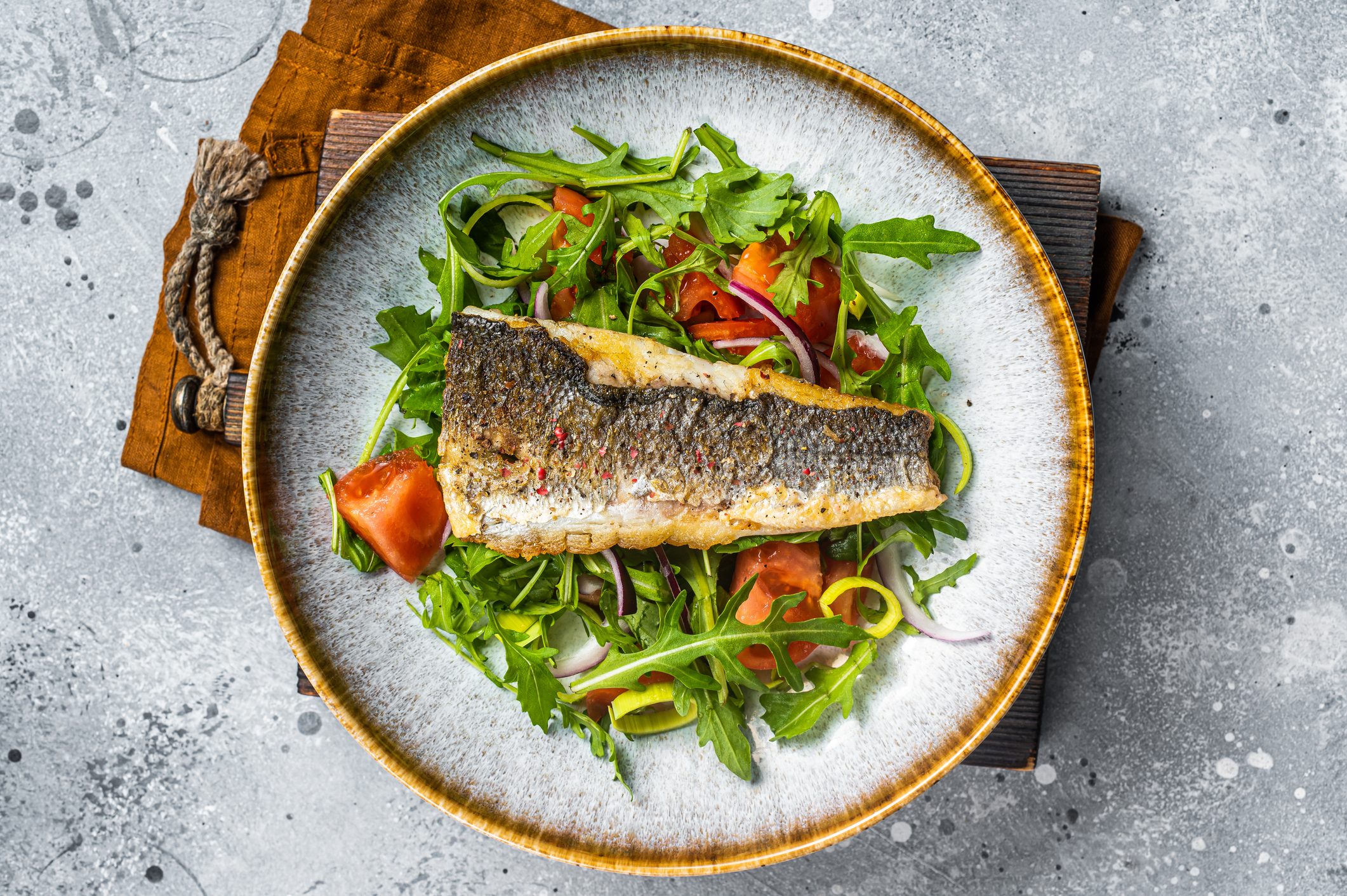 Fried sea bass fillet with vegetable salad, Dicentrarchus fish. Gray background. Top view