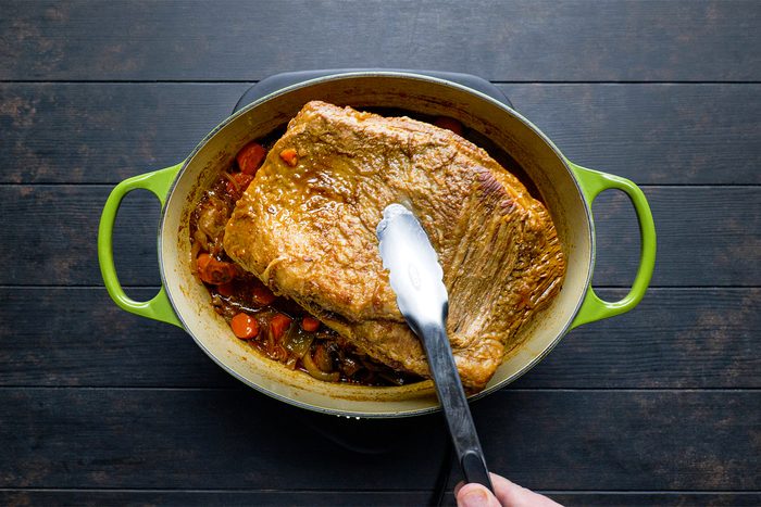 A person holding a spatula over a large piece of meat