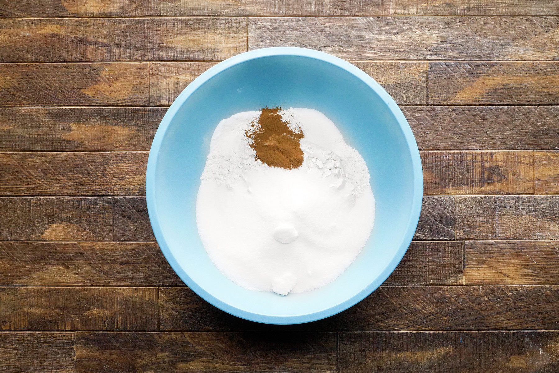 Mixing together flour, sugar, salt in a large bowl on a wooden table