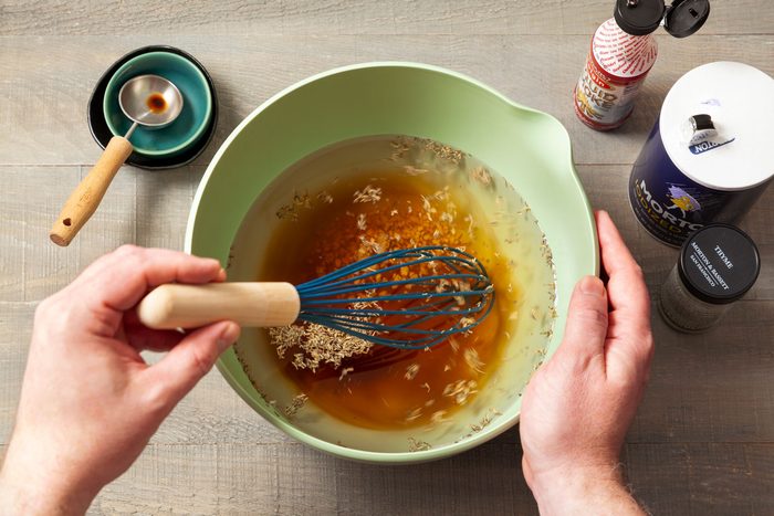 in large green bowl mixing water, brown sugar, salt, liquid smoke, garlic and dried thyme with whisk on wooden surface