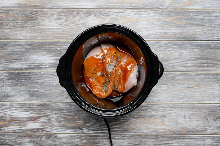 Chicken breasts with hot sauce and pepper mixed in a slow cooker.