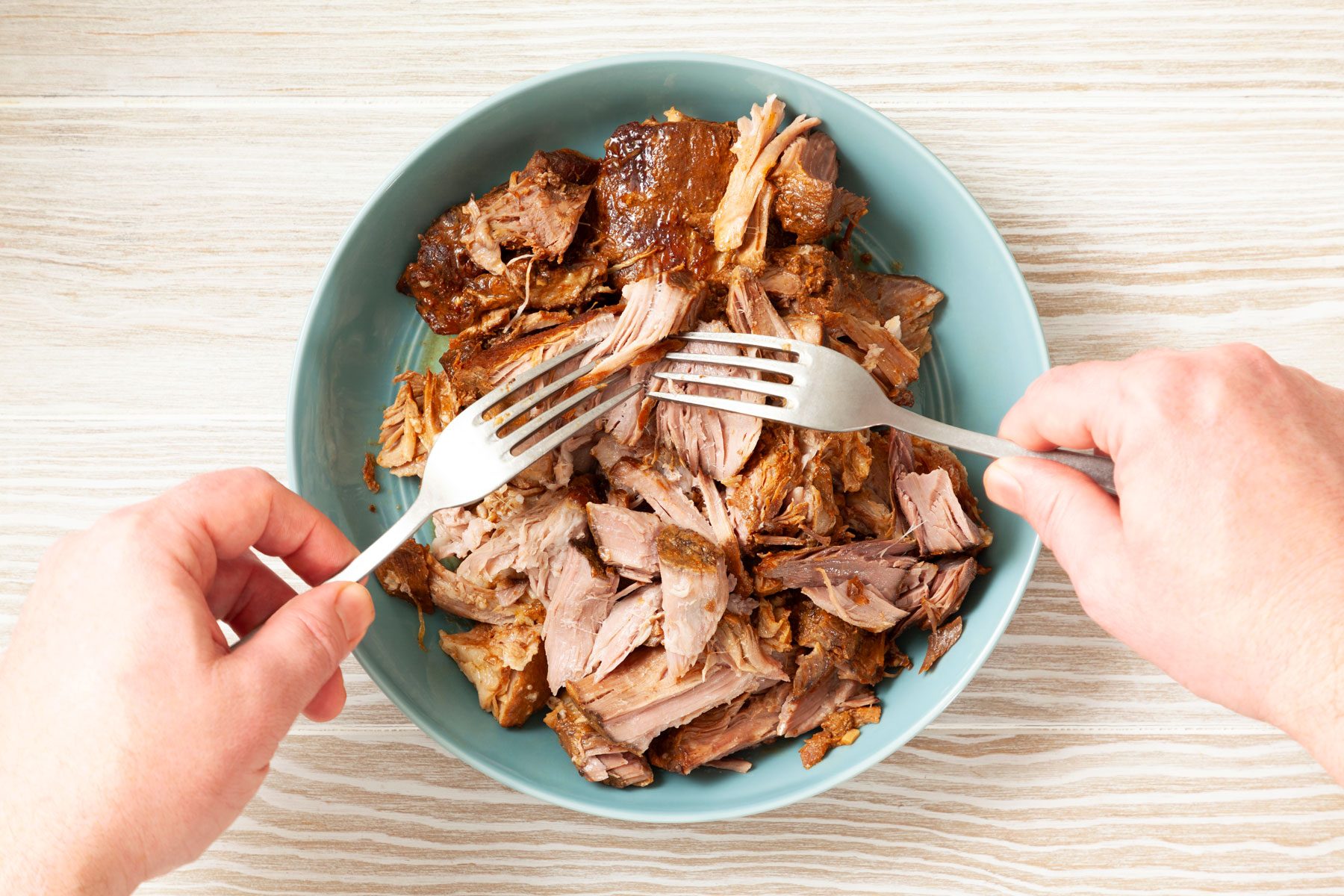 Shreding the roasted pork with a fork in a small bowl