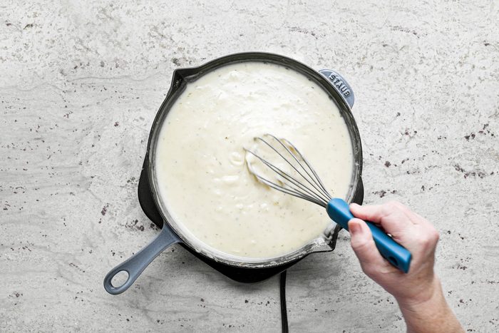 Stirring the mixture with spatula in a large skillet on a marble countertop.