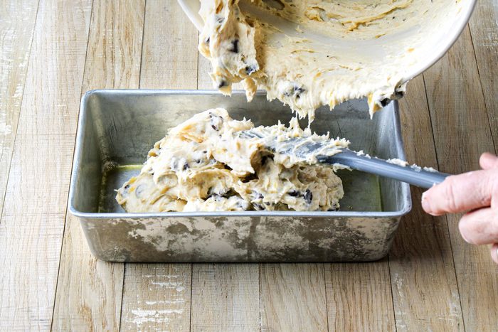 Pouring the Chocolate Chip Banana Bread batter into a loaf pan placed on a wooden surface
