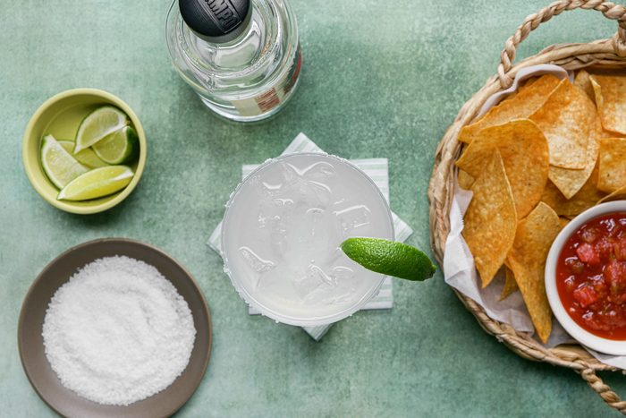A glass of classic margarita with lime wedges and chips