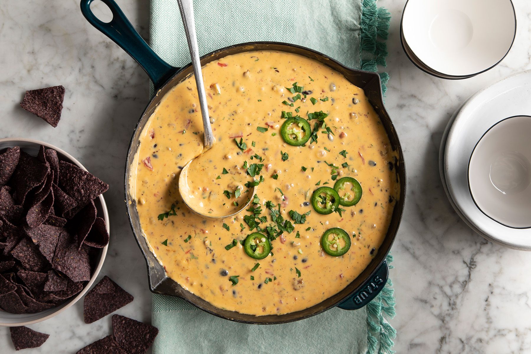 Cowboy Queso in skillet with taco chips and white empty bowls