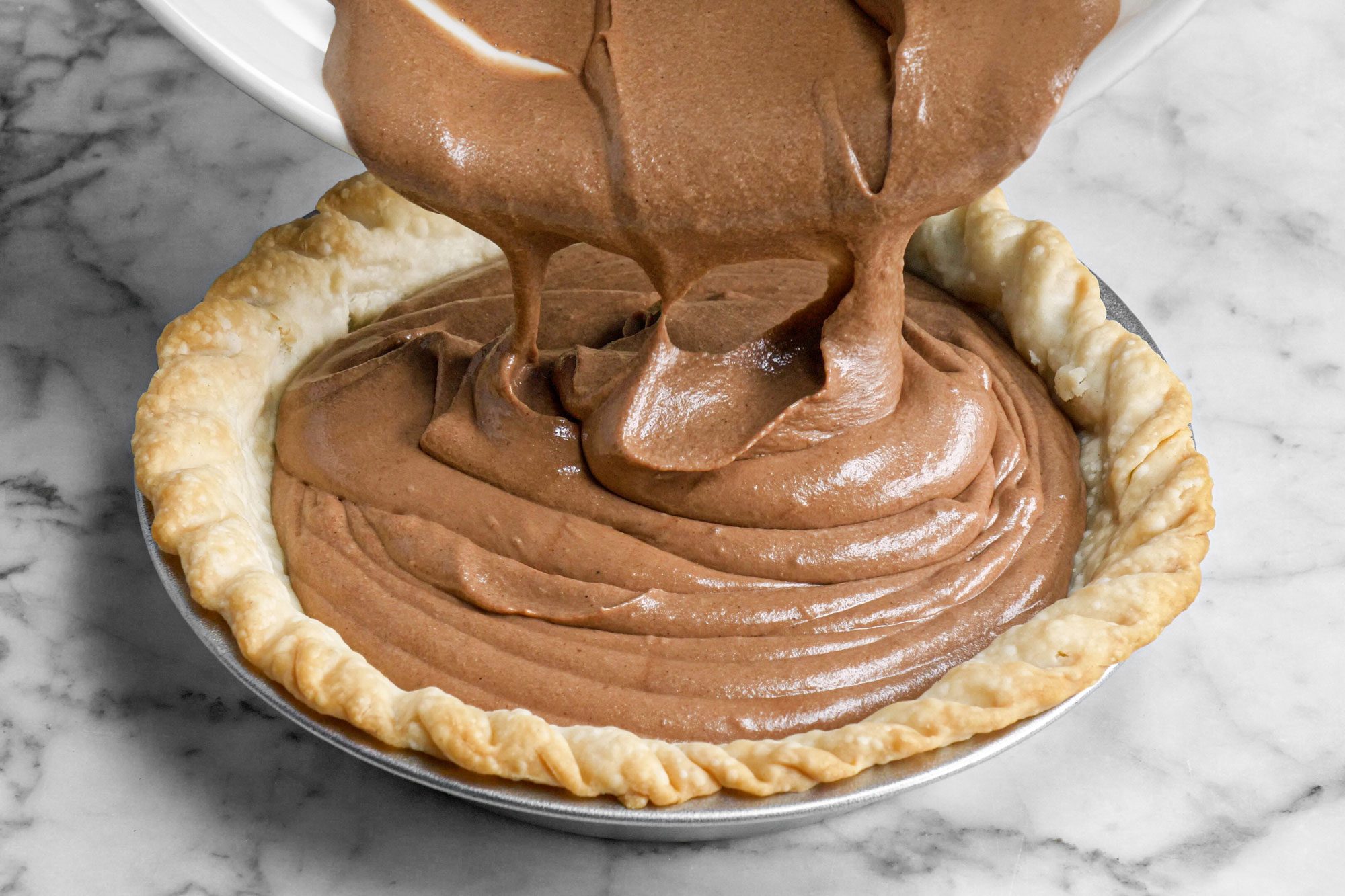 pouring chocolate mixture into a pie crust, marble background