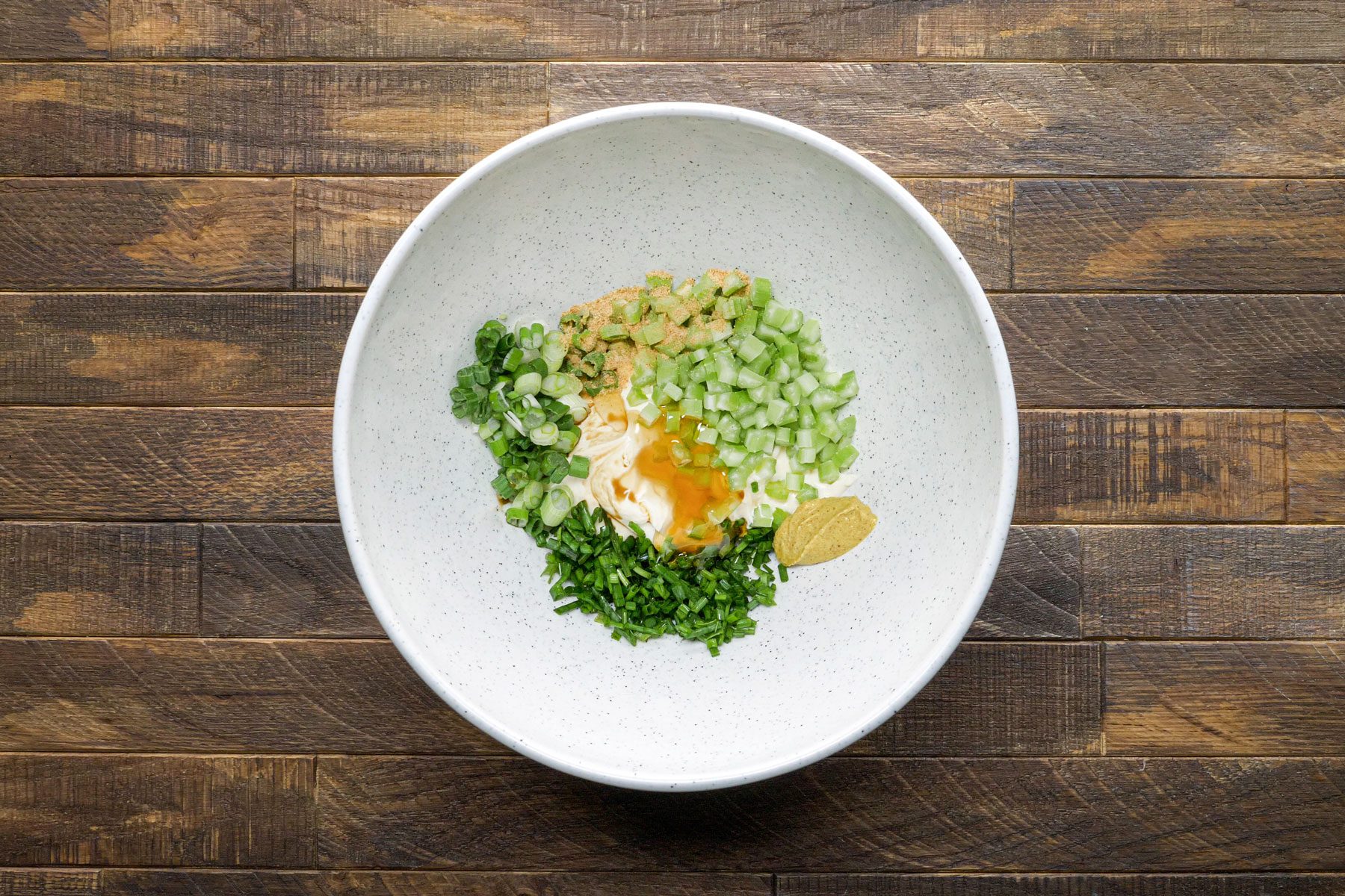 Mixing together mayonnaise, celery, green onions, chives in a large bowl.