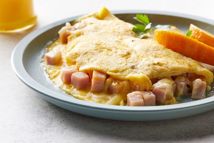 Ham And Cheese Omelet served on plate with orange slices and juice glass on side