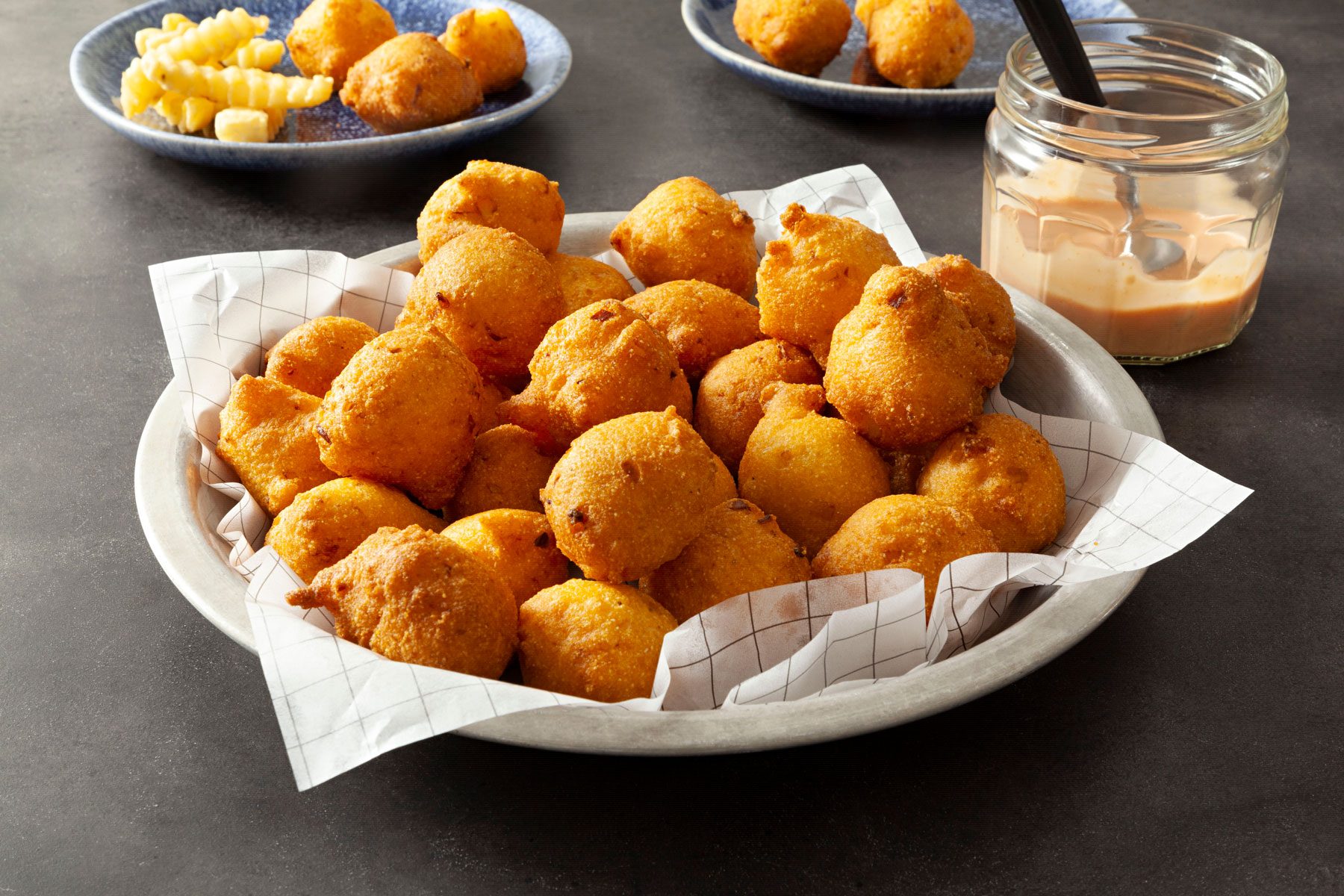Hush Puppies served in a plate with sauce on a grey marble countertop.