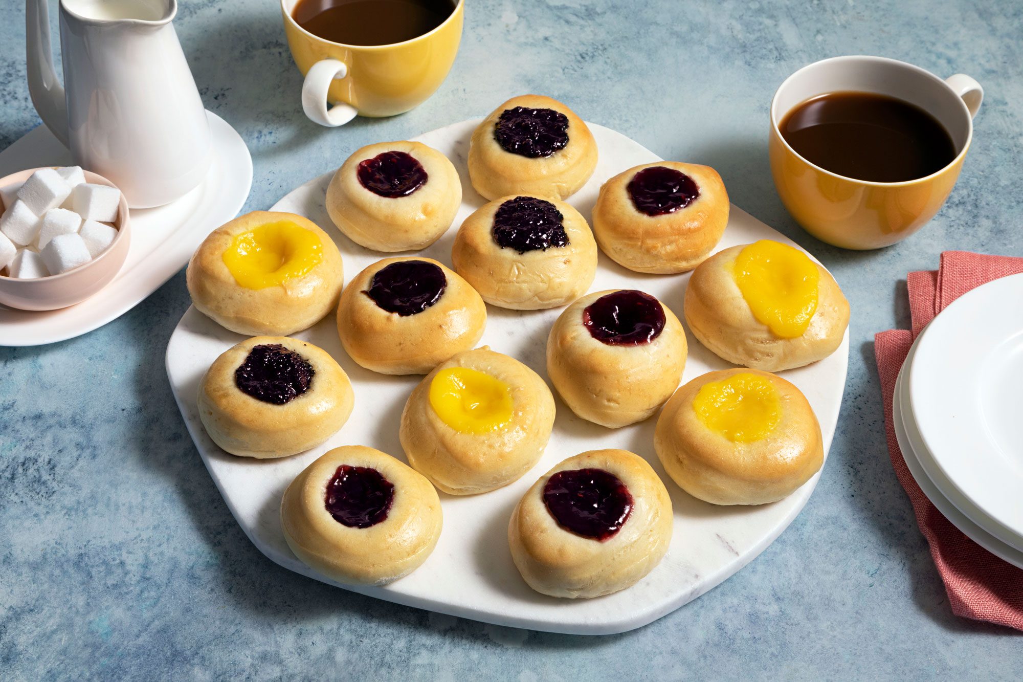 Kolaches on a marble plate and a cup of hot chocolate placed next to it
