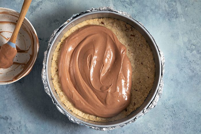 Adding the chocolate mixture over baked crust in baking tray