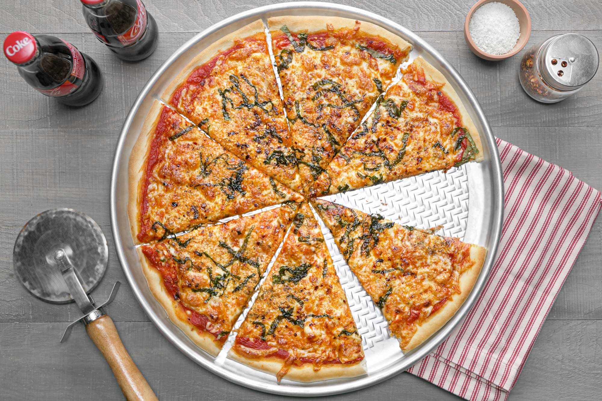 Sliced New York-Style pizza with crispy thin crust, melty cheese, flavorful toppings, and coke on the side