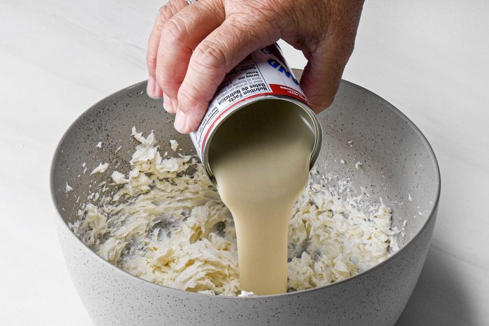 a person pouring sweetened condensed milk in large bowl on marble surface