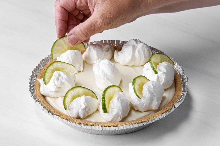 a person topping the pie with whipped cream and lemon slices on marble surface