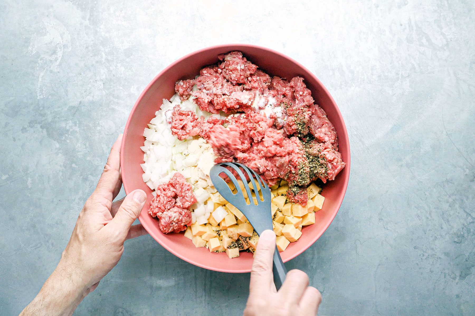 Mixing chopped potato cubes, minced meat and vegetables in a bowl