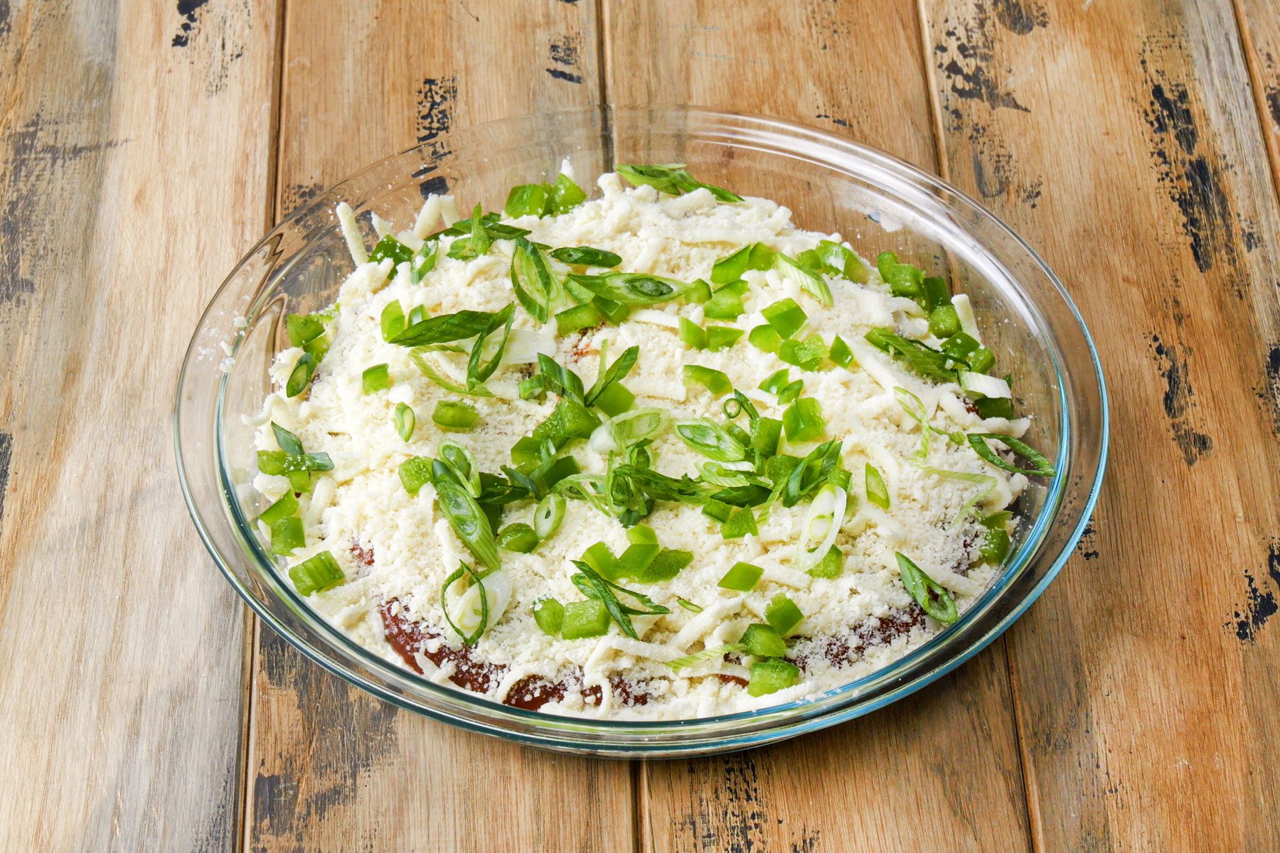 chopped green peppers and onion on cheese and pizza sauce in a large bowl