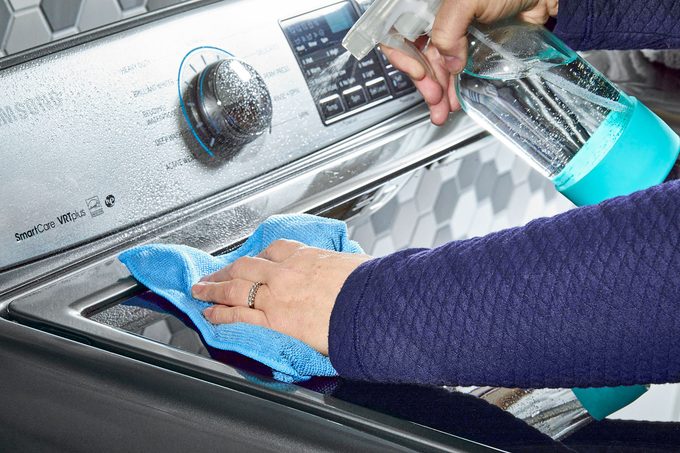 Lady cleaning outer side of washing machine with micro fibre cloth and cleaning spray