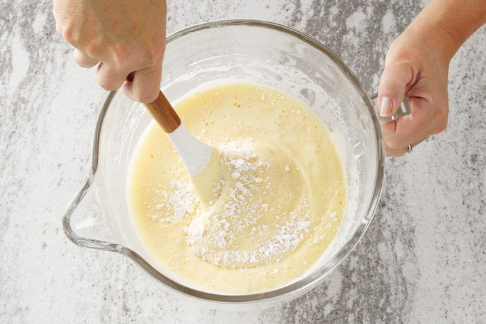 overhead shot; white textured background; Folding flour mixture gently into egg mixture with spatula;