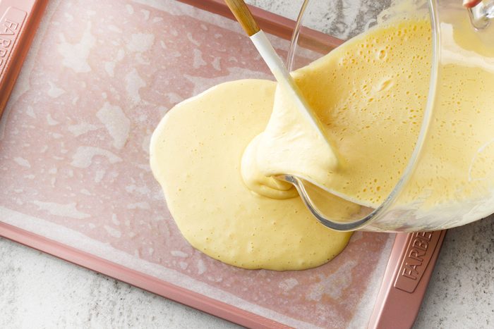 tilted shot; white textured background; Spreading roll cake batter onto a greased jelly roll pan;