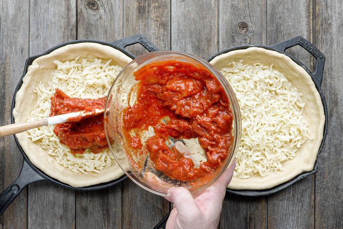 Adding tomato sauce over cheese sprinkled dough on skillets