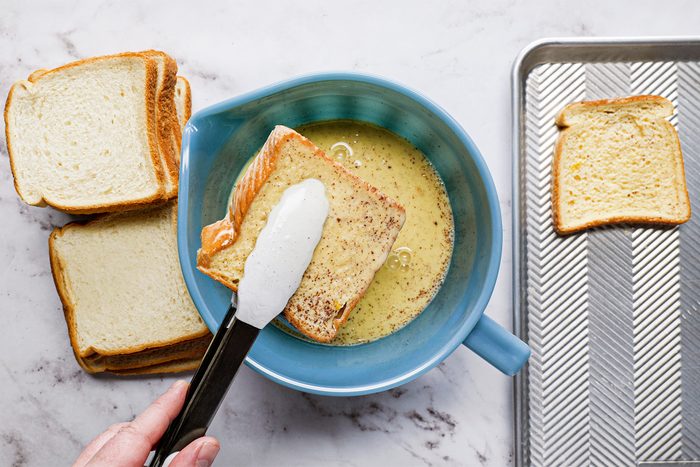 A person holding a knife over a bowl of bread, preparing to slice it for a meal