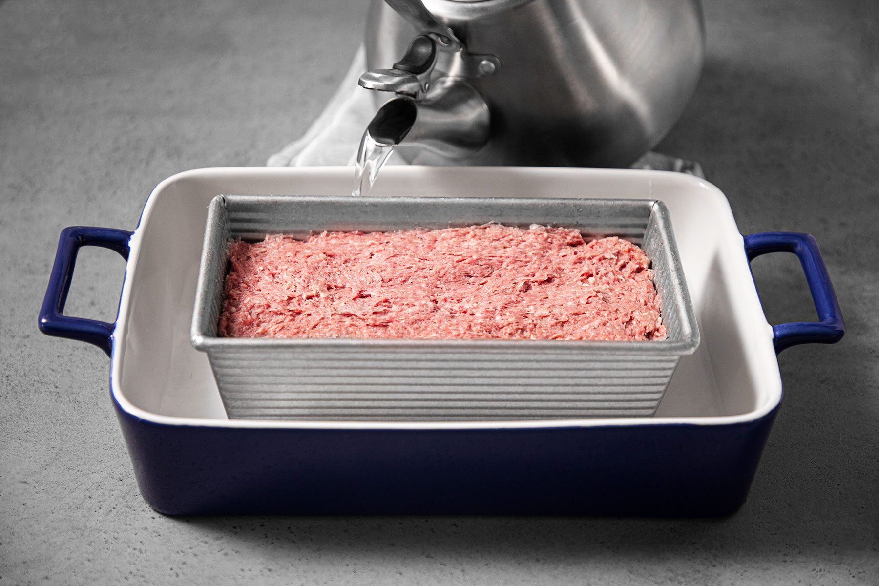 Pouring water in bigger pot with baking dish in it.